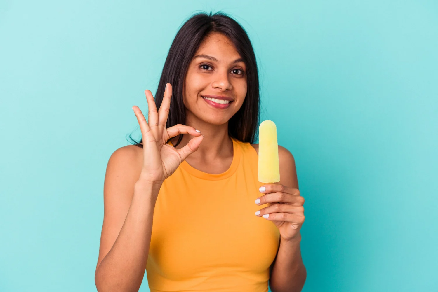 Mulher sorrindo com picolé amarelo na mão e consumindo os beneficios do sorvete