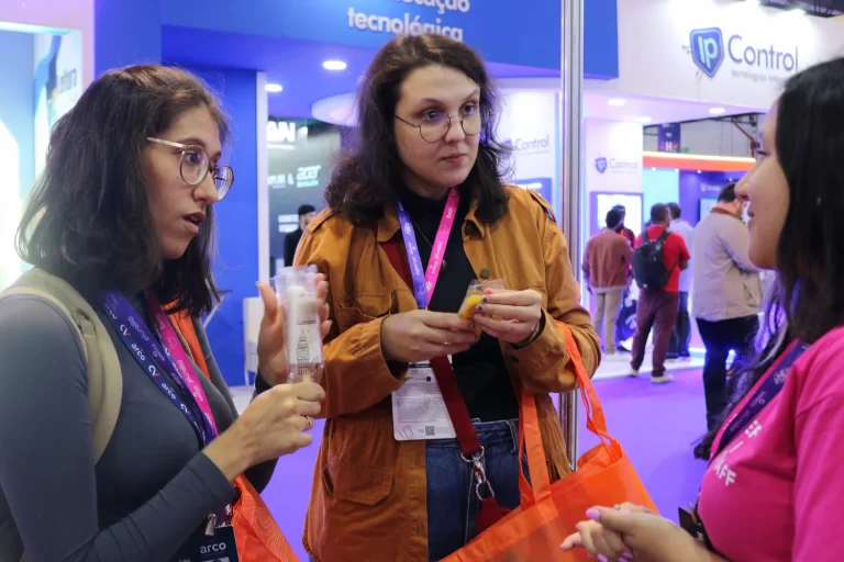 Promotora interage com clientes em evento enquanto entrega brindes de marketing personalizado.