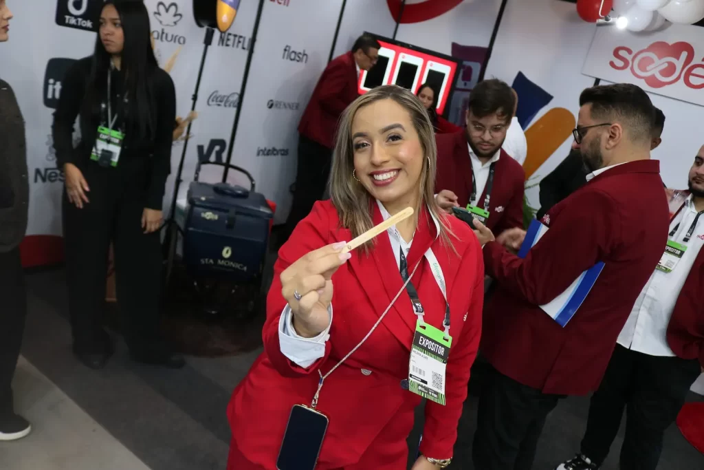 Promotora sorri e segura palito de picolé personalizado em evento sobre branding emocional